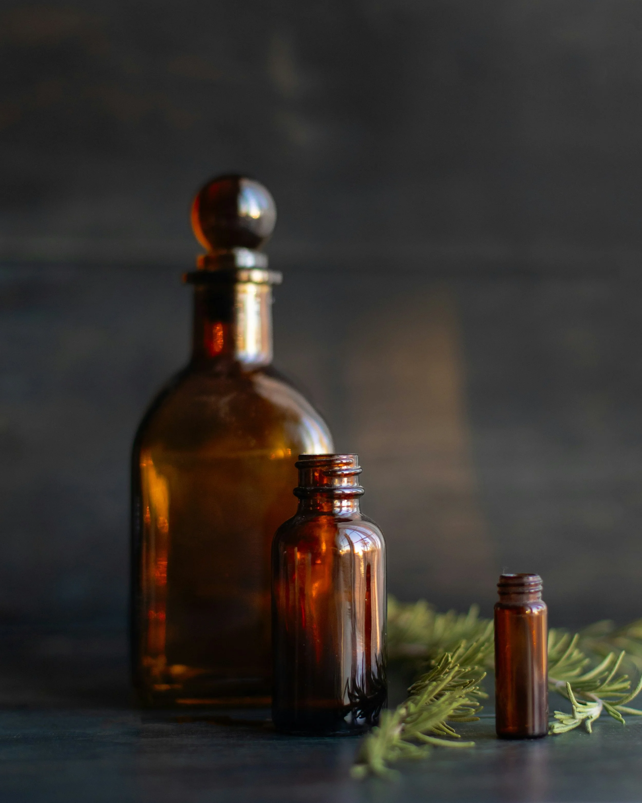 Gouttes d'huile dans des petits flacons en verre ambré, avec des branches de sapin vert en premier plan, sur fond sombre.