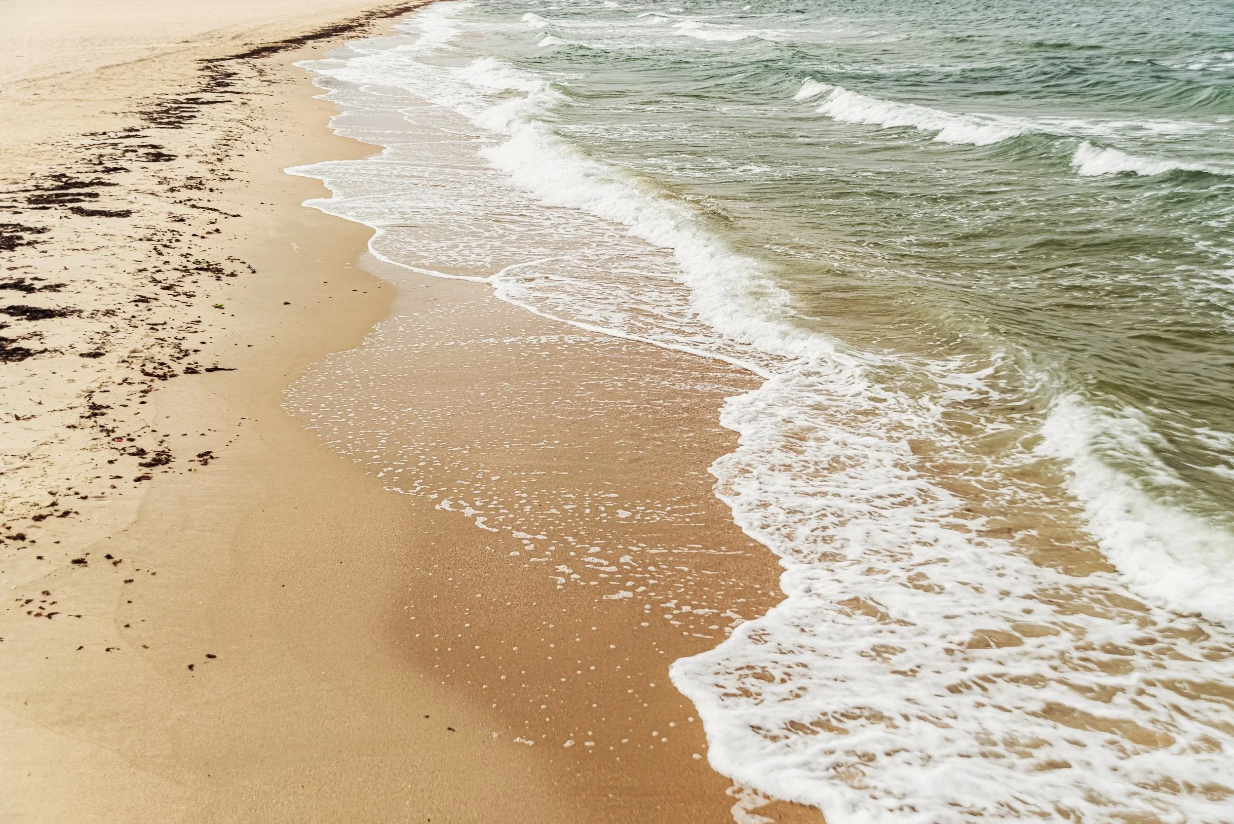 Plage de sable avec vagues doucement qui se brisent sur le rivage.