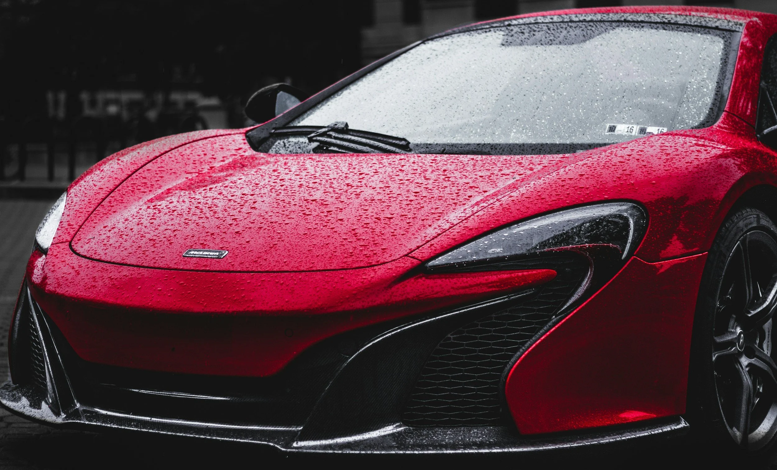 A red sports car with rain droplets on its surface, parked outdoors during rainy weather.