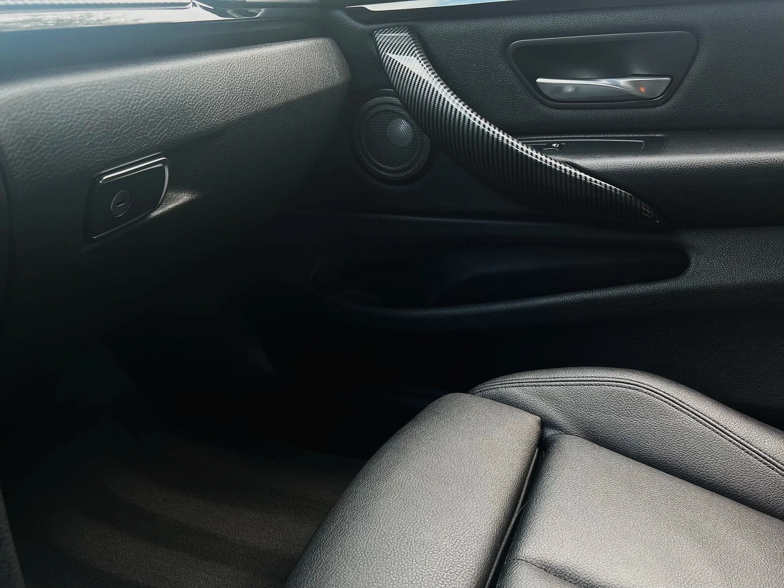 Interior of a car showing the passenger side, including the dashboard, door panel with a speaker, and a black leather seat.