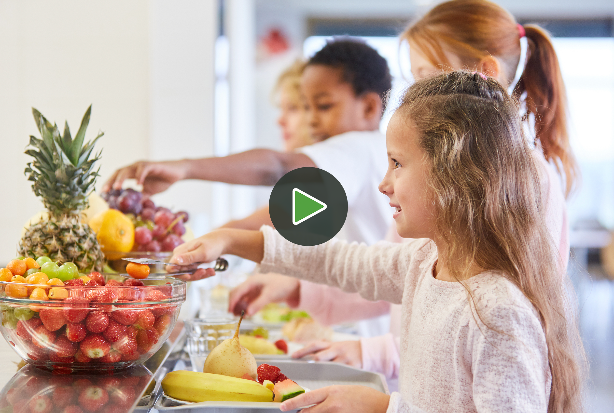 Children selecting fruit at a buffet table with pineapples, strawberries, grapes, bananas, and other fruits.