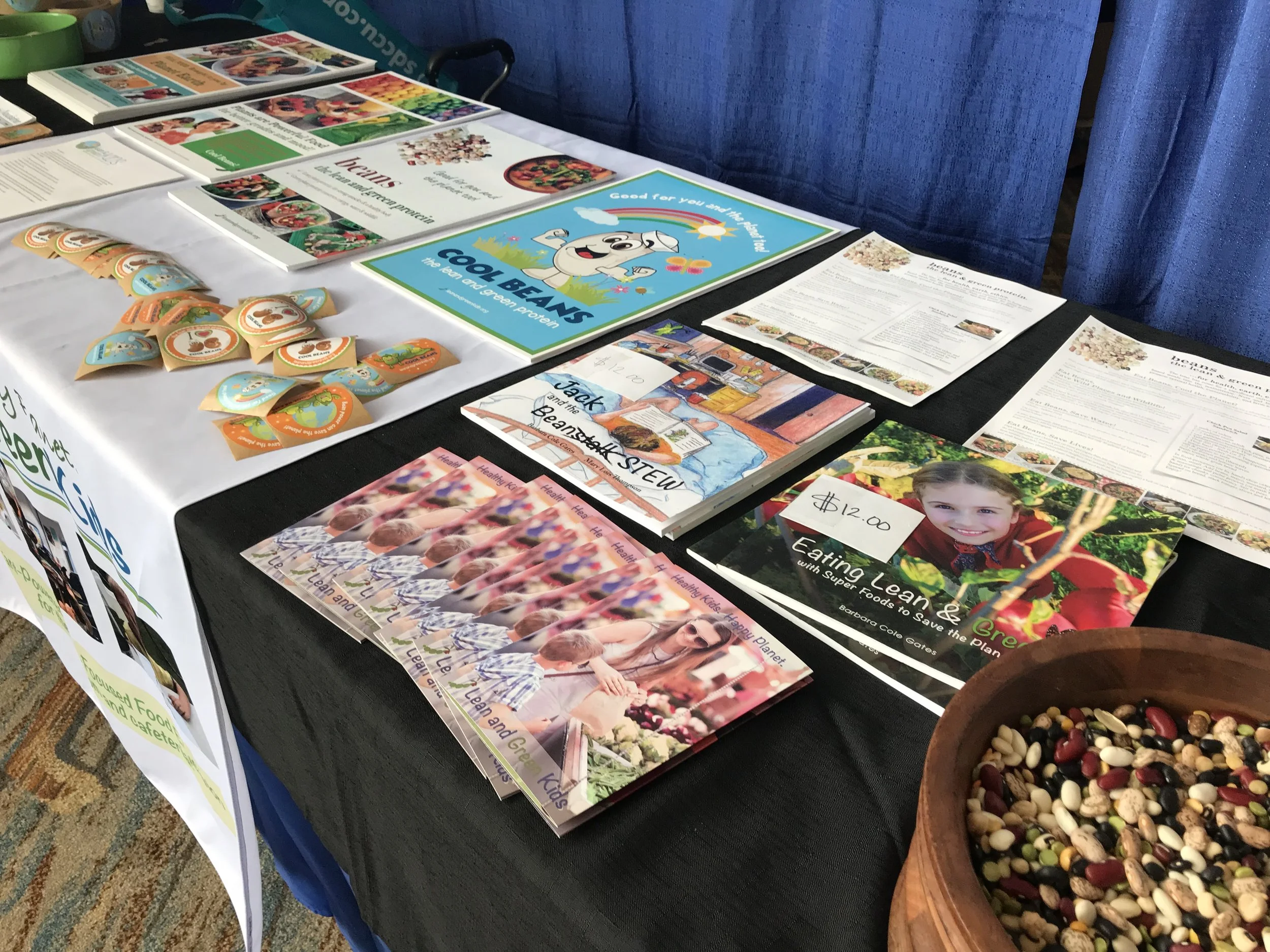 Table with brochures and pamphlets about healthy eating and greens, a bowl of mixed beans, and a photo of smiling children at the bottom.