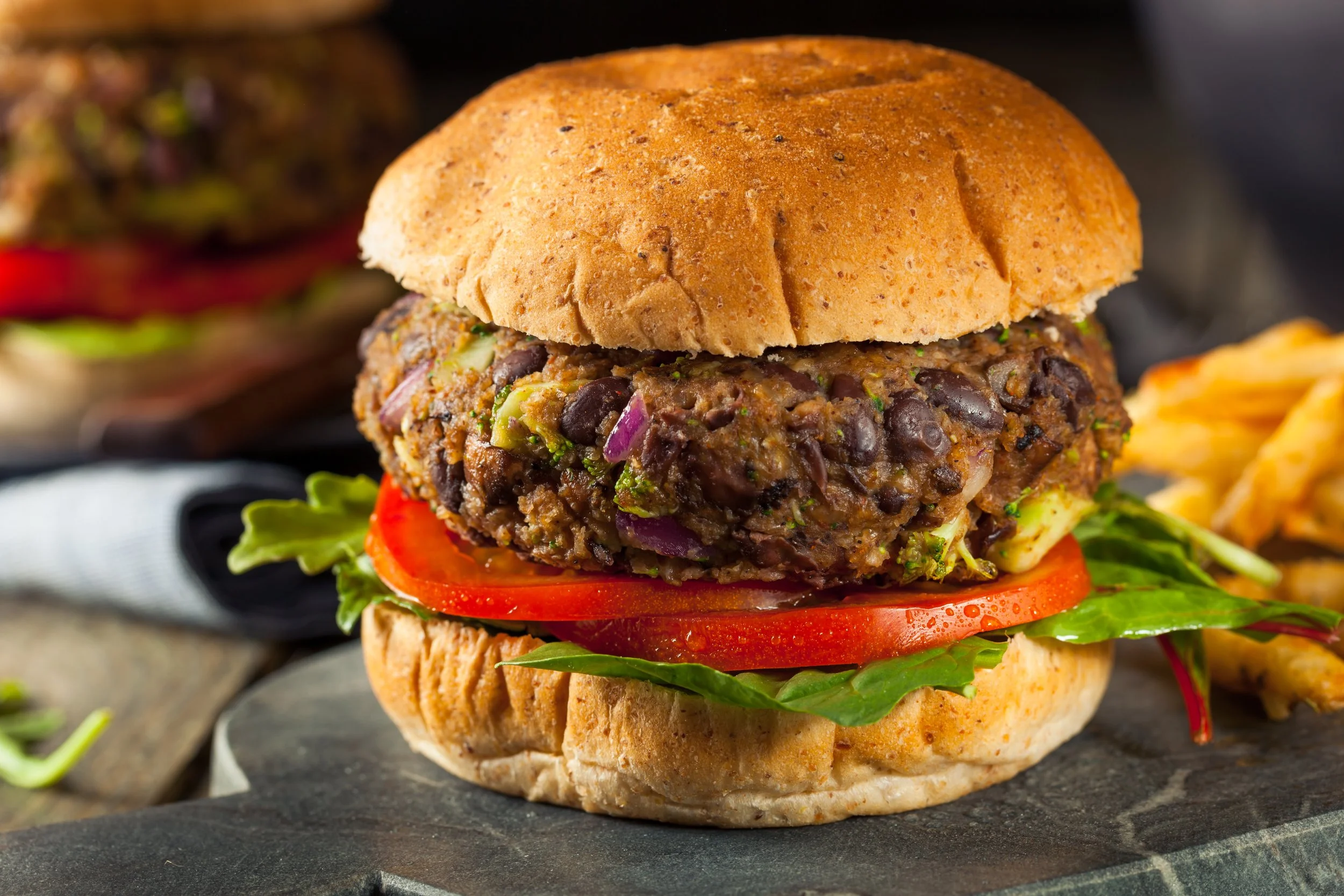 Close-up of a veggie burger with a whole wheat bun, layered with lettuce, tomato slices, red onion, black bean patty, and topped with the top bun.