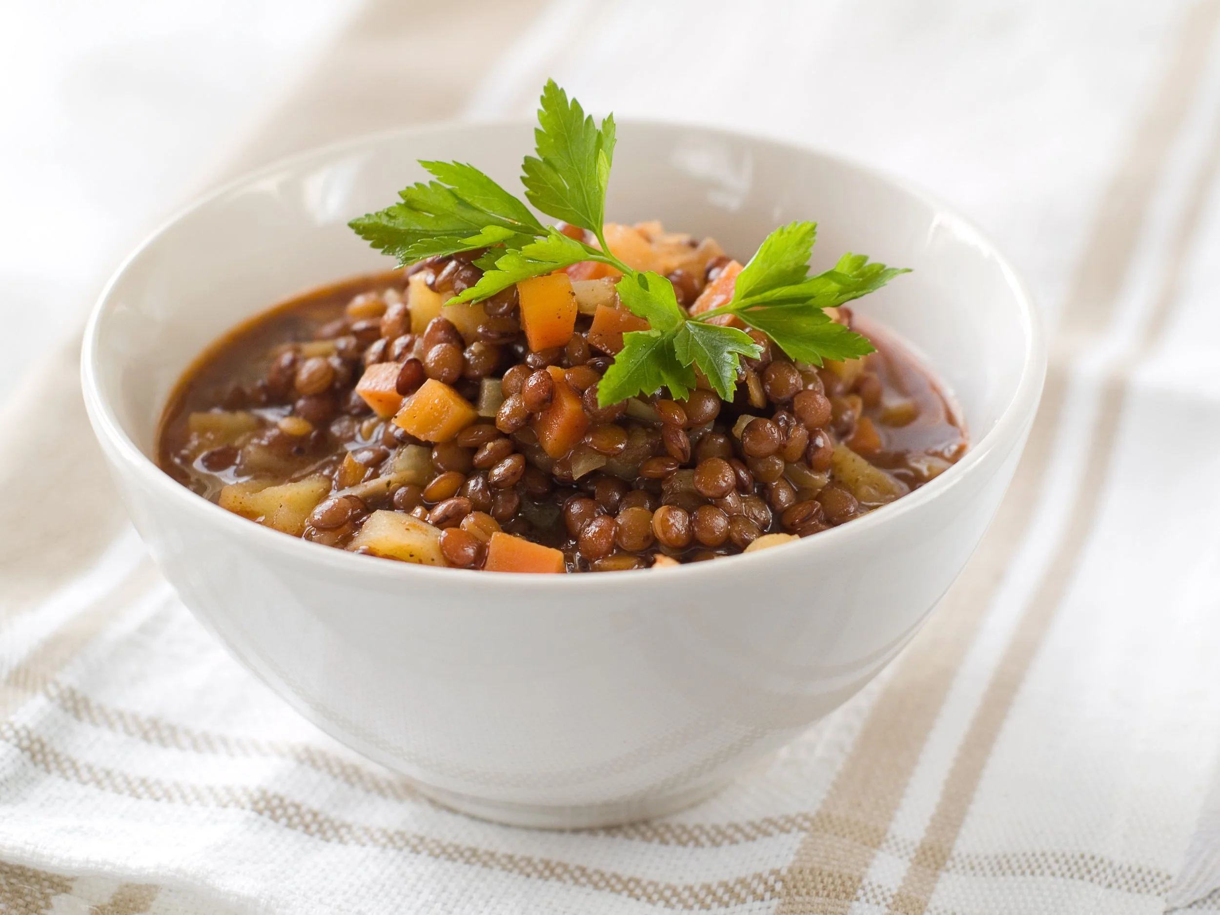 A bowl of lentil soup garnished with parsley on top.