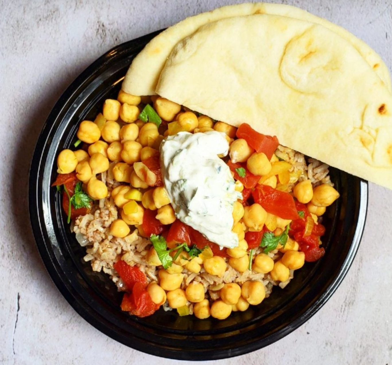 A close-up of various dried legumes and vegetables, including garlic bulbs, a carrot, chickpeas, lentils, split peas, and a bowl of vegetable soup containing chickpeas and carrots.