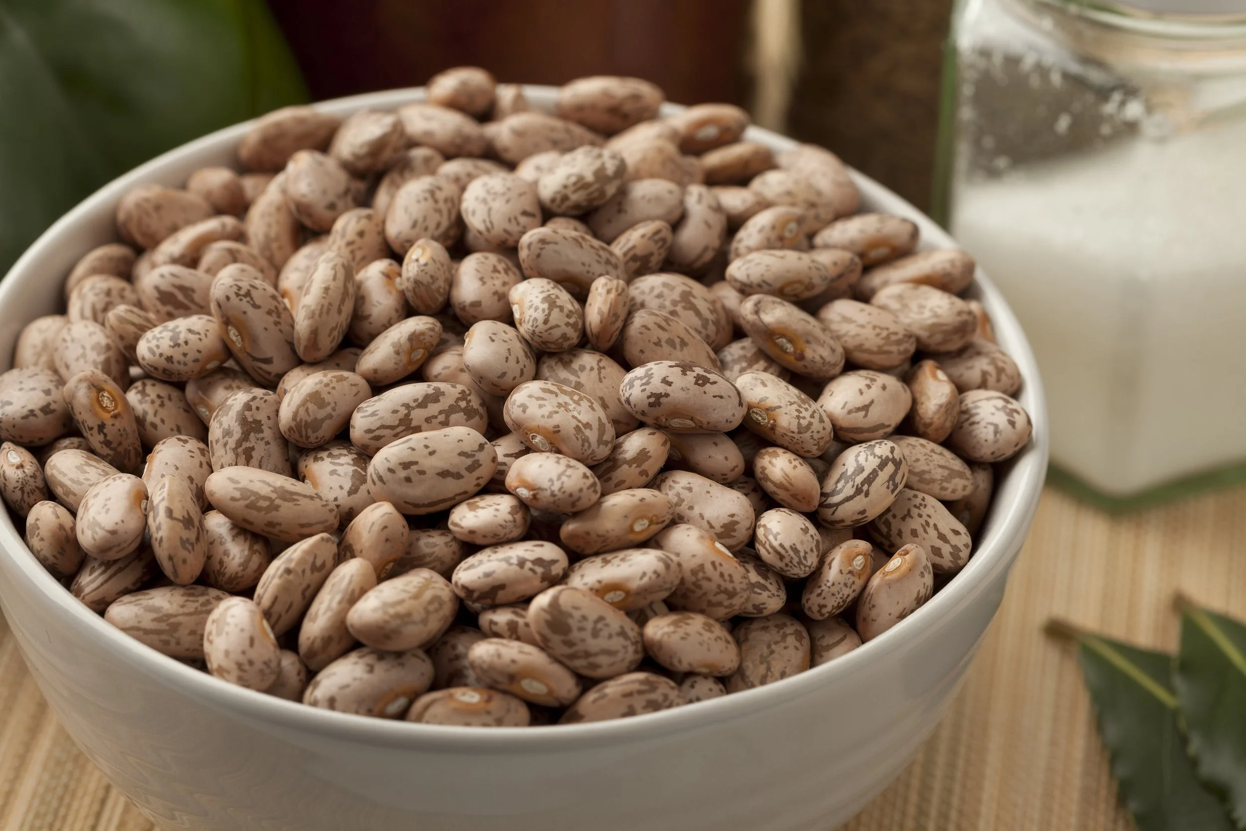A white bowl filled with pinto beans on a wooden surface.