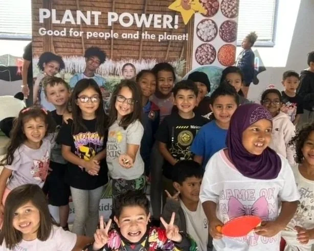 Group of children smiling and posing for a photo in front of a banner that says 'PLANT POWER! Good for people and the planet!'