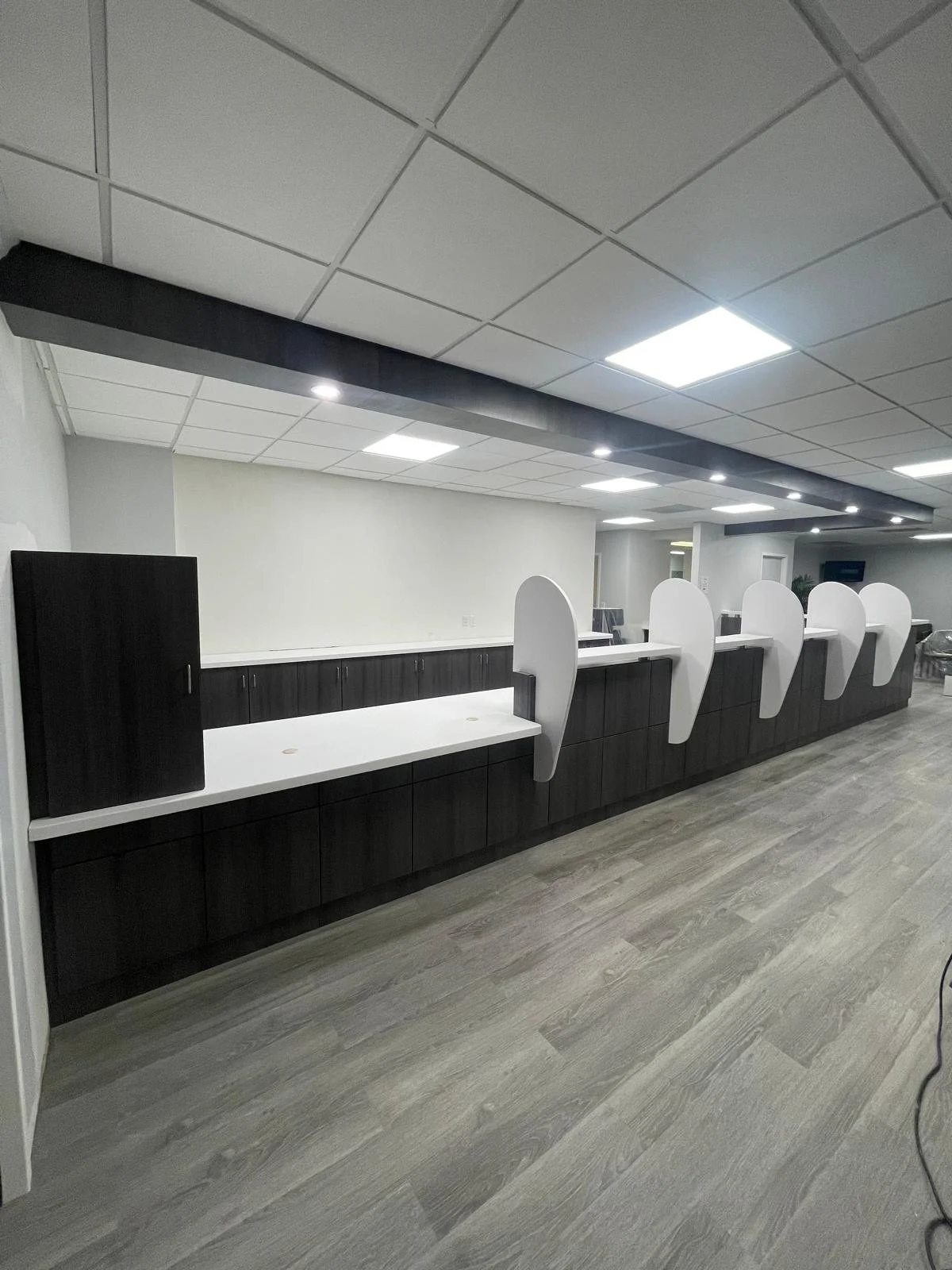 A modern office reception area with a long black counter featuring white curved dividers, overhead fluorescent lighting, and laminate wood flooring.