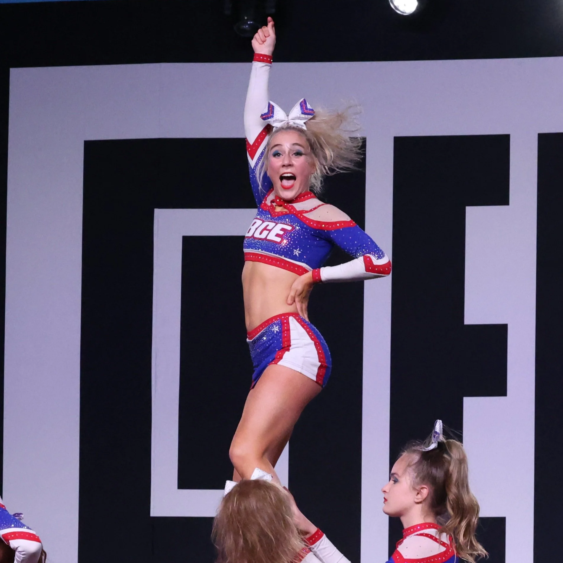 Cheerleader in red, white, and blue costume performing a stunt during a cheerleading routine.