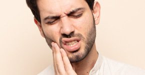 Homem com expressão de dor, segurando o queixo com a mão