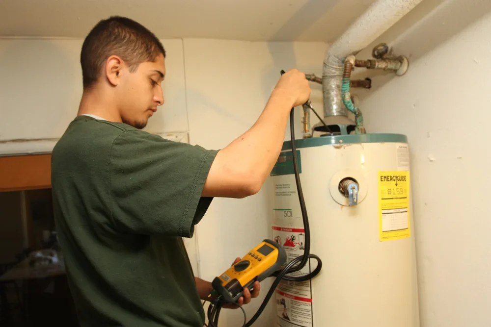 A young CSET technician using a digital multimeter to test electrical wiring on a home water heater.