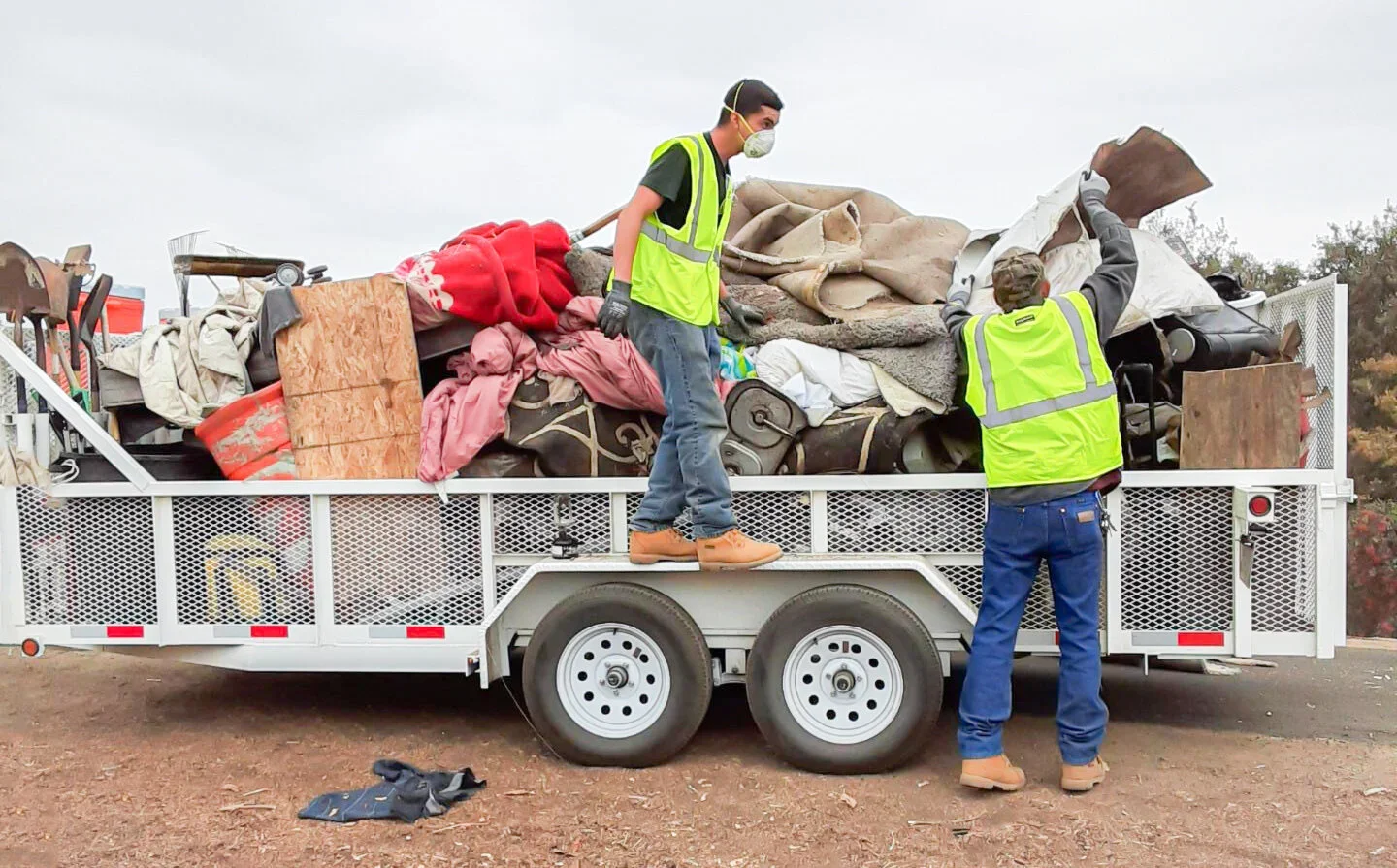 CSET workers in safety vests loading discarded mattresses, wood, and debris onto a large flatbed trailer during a community cleanup.