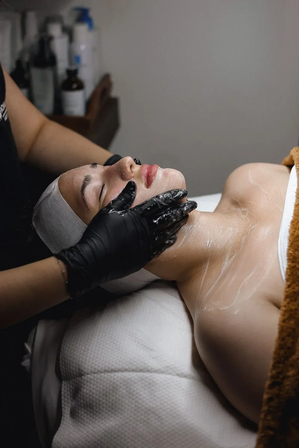 A woman receiving a facial treatment while lying down on a bed with her eyes closed.