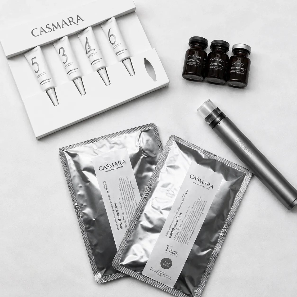 Skincare products from Casmara, including tubes labeled 5 to 6, small bottles labeled Lightening, a silver spray bottle, and silver foil packets on a white surface.