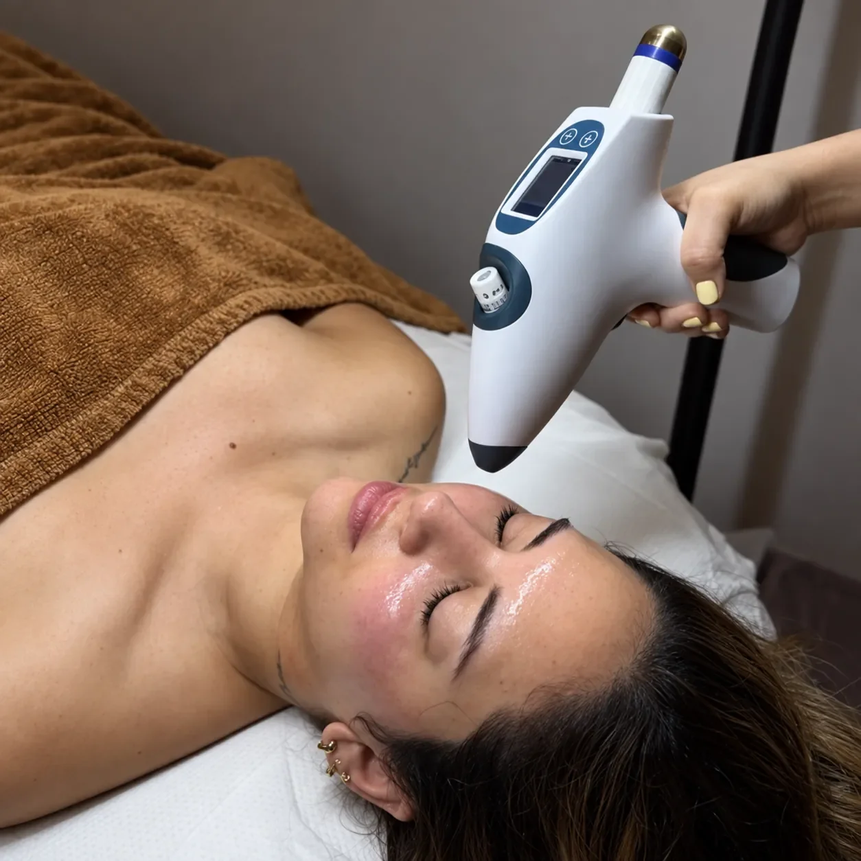 A woman lying on a bed receiving a facial treatment with a handheld device.