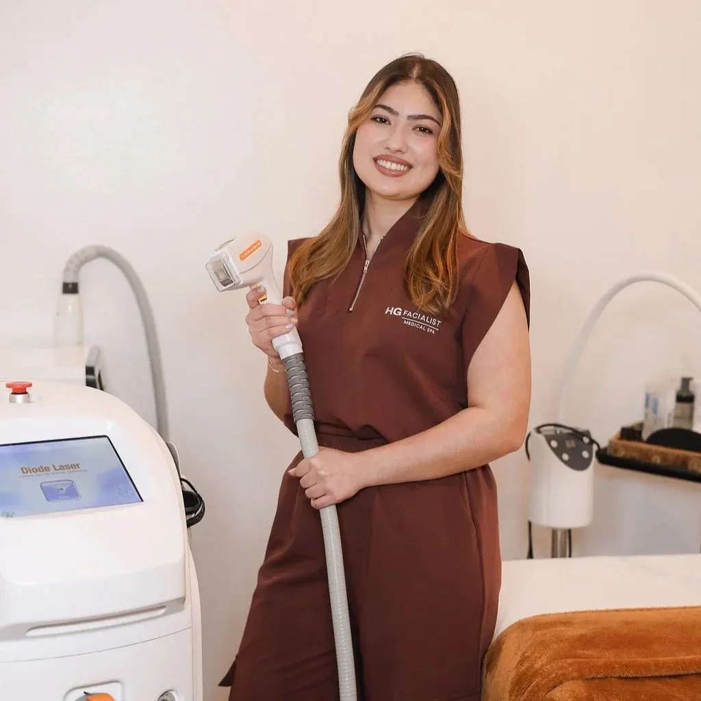 A smiling woman in a brown uniform holding a laser treatment device in a skincare clinic.