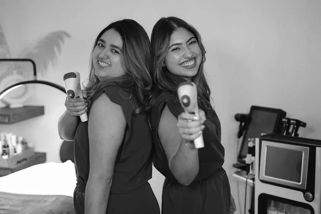 Two women smiling and holding infrared thermometers back to back in a medical room
