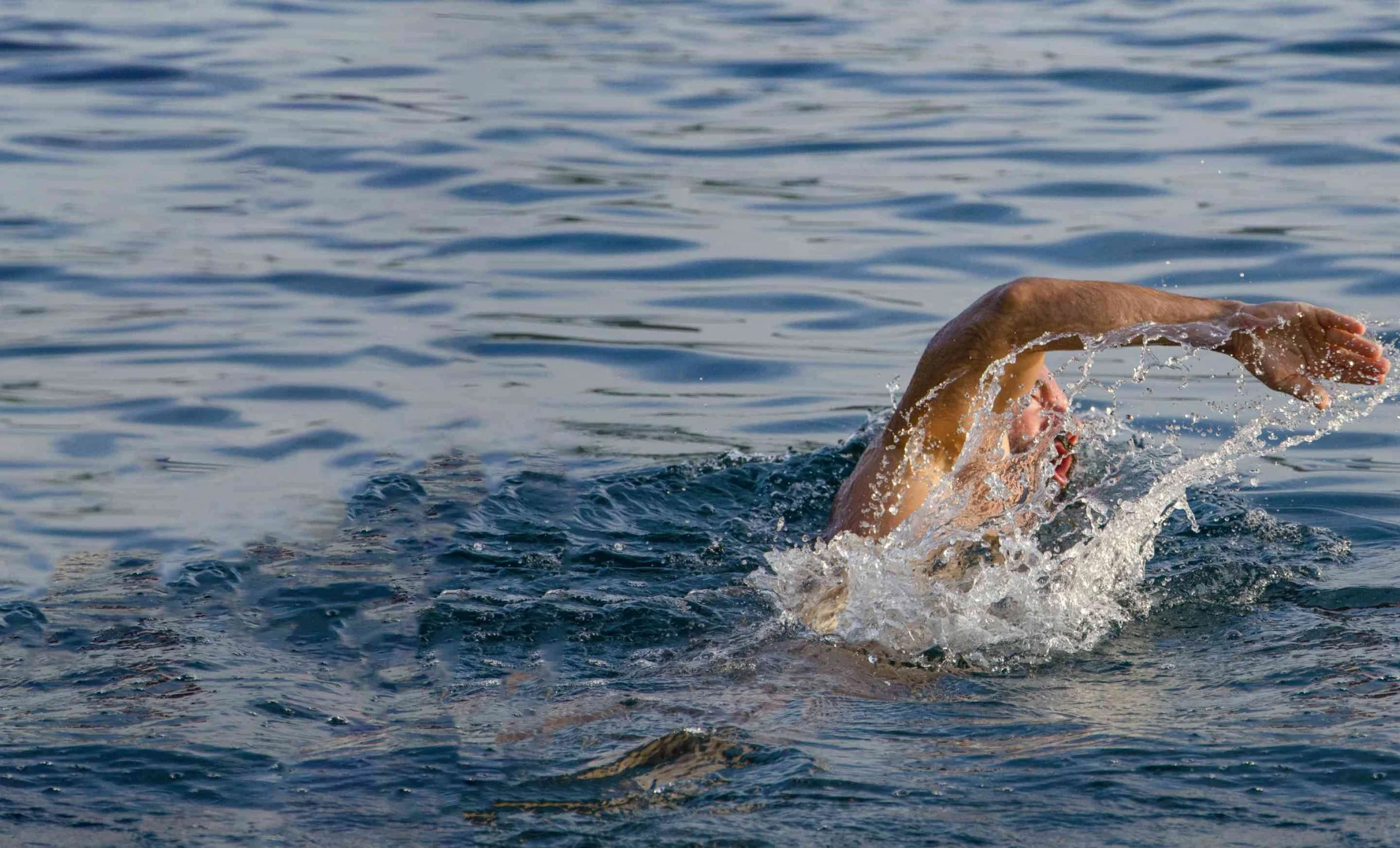 A person swimming in open water, performing a freestyle stroke with their arm out of the water.