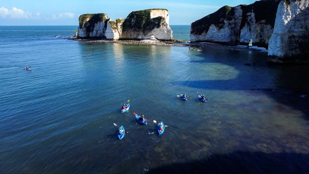 Group of people kayaking besides Old Harry's rocks near sandbanks and Studland in Poole. Clear blue skies over head, clear ocean water with people having a good time
