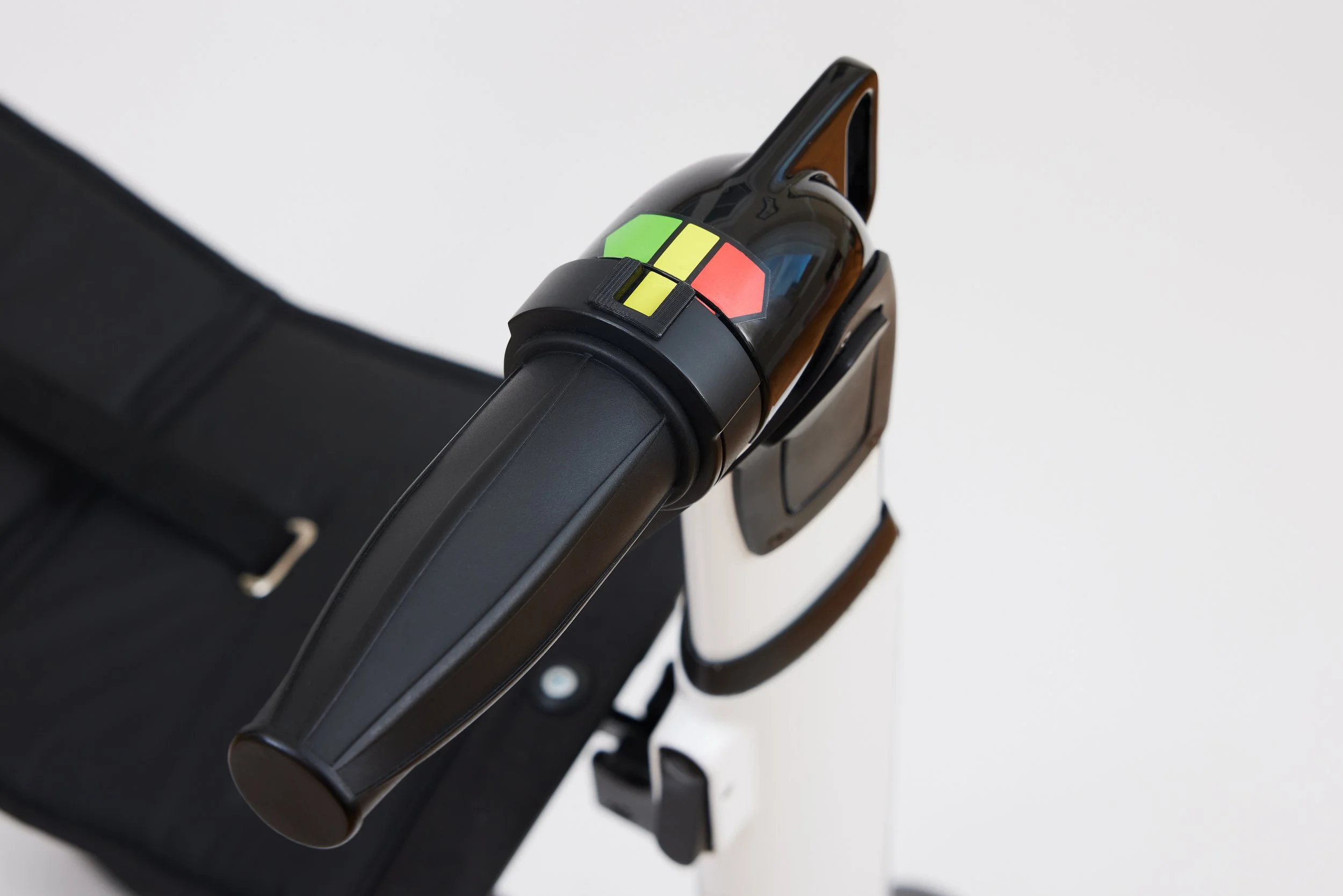 Close-up of a black automatic hand sanitizer dispenser mounted on a white stand, with a black suitcase nearby, against a white background.