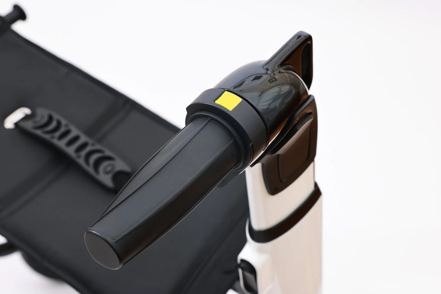 Close-up of a black automatic hand sanitizer dispenser mounted on a white stand, with a black suitcase nearby, against a white background.