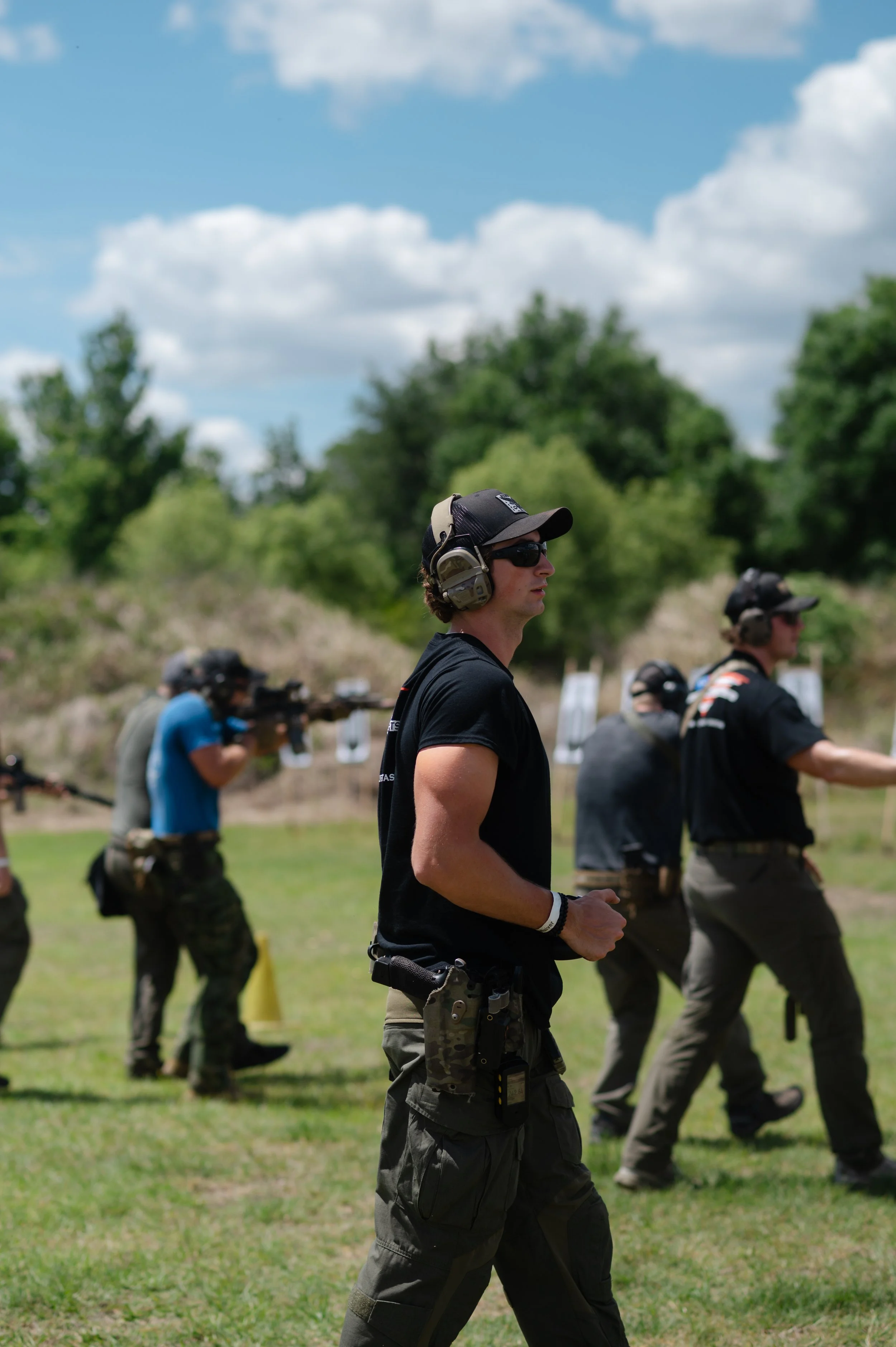 A man in military gear with a helmet and tactical vest, sitting on a table in an indoor military or tactical environment, engaging in conversation with another person.
