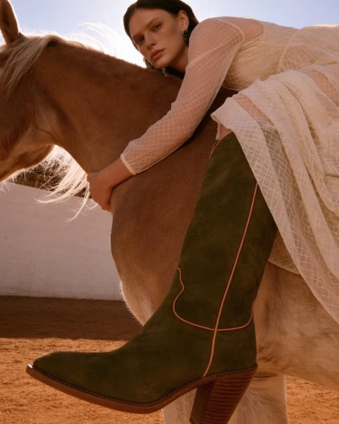Close view of an olive suede boot against a horse