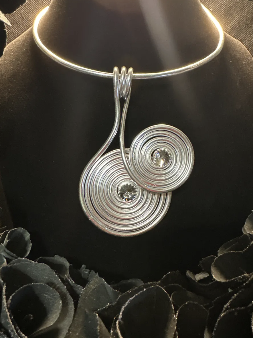 Silver jewelry set consisting of a necklace and matching earrings displayed on a black bust, with black decorative roses at the base.