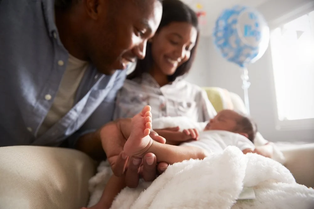 Family at home, with a man, woman, and baby, celebrating a special occasion with a blue birthday balloon in the background.