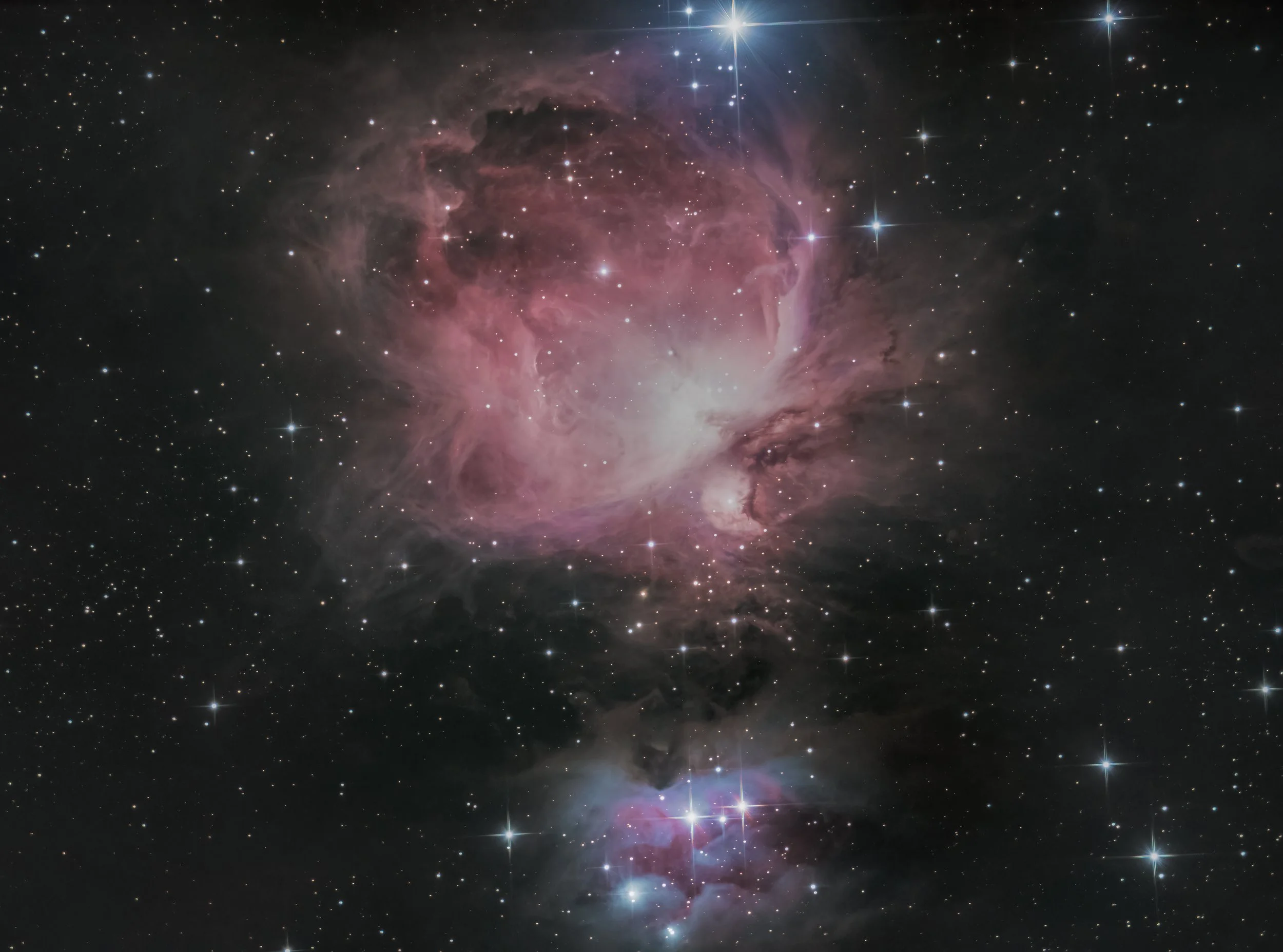 A colorful nebula with pink, purple, and white clouds of gas and dust in space, surrounded by numerous stars.