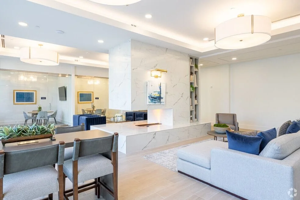 Modern lounge with white walls, beige floors, comfortable seating, and decorative lighting. The coworking club space in an Apartment complex.