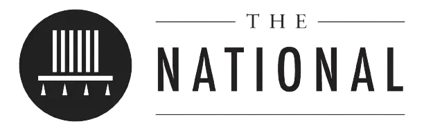 The logo of The National, featuring a circular emblem with vertical lines and smaller symbols underneath, with the text 'The National' to the right.