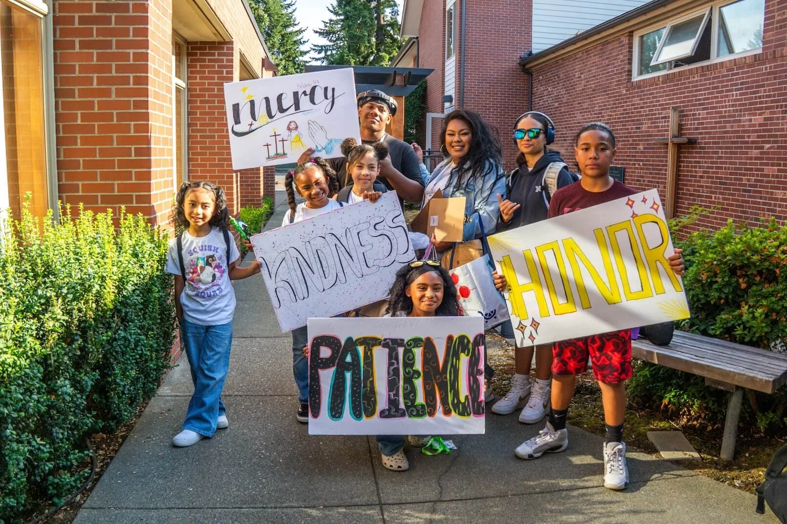 A group of summer camp students and leaders holding signs that say “honor,” “kindness,” “mercy,” and “patience.”