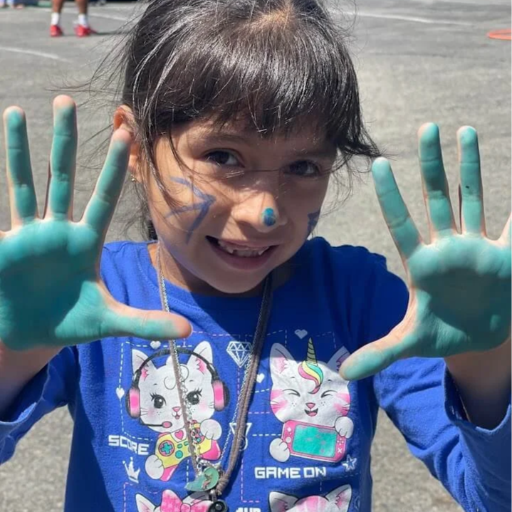 A summer camp student flashes her hands, both painted bright blue, after completing an art project.