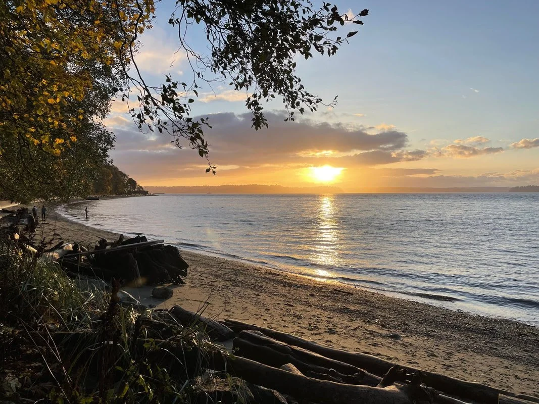 A fall sunset stretches over the Salish Sea looking out at Vashon Island from Lincoln Park in West Seattle after a Wild Church event.