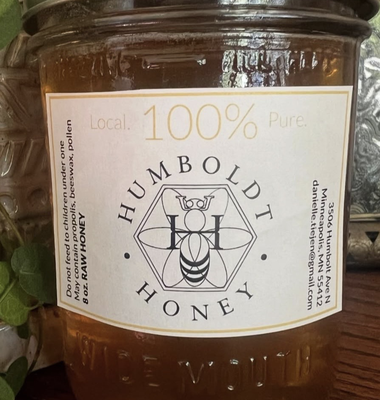 A jar of honey labeled 'HUMBOLD HONEY' featuring a bee and geometric design, indicating it is 100% pure, local, and raw honey.