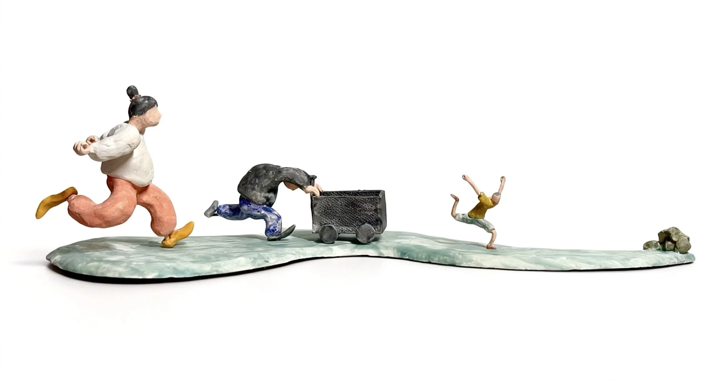 Colorful ceramic sculpture of four people running and playing on a flat surface with rocks, one pushing a cart, and a person falling.