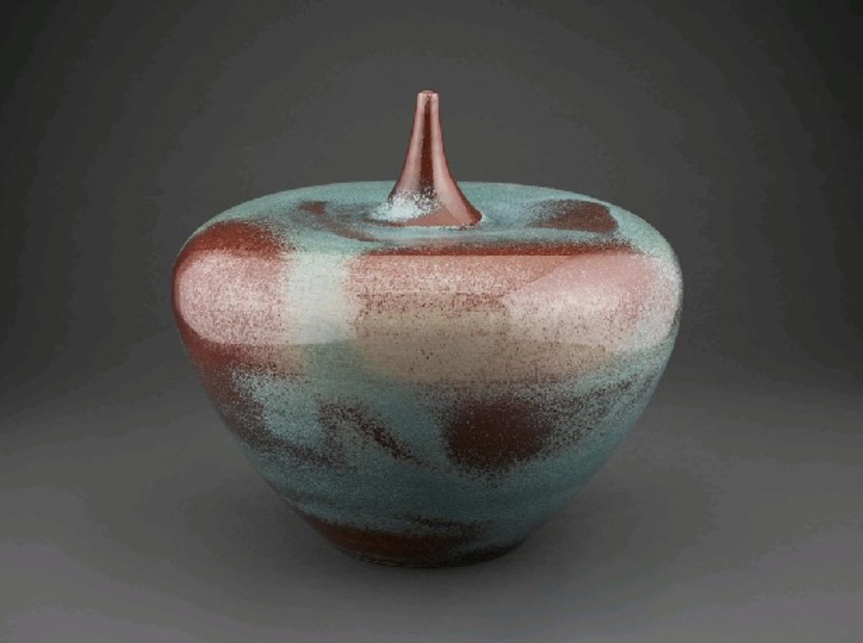 Colorful ceramic vase with a lid, featuring an abstract pattern of red, blue, and beige, with a pointed finial on top.