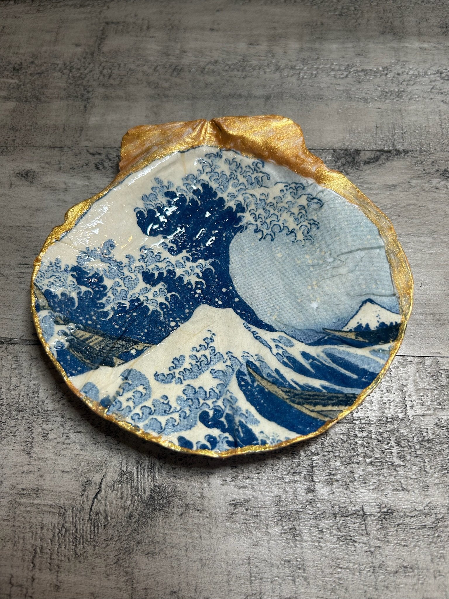 A decorative ceramic plate with a blue wave design, gold trim, and a partial view of a mountain in the artwork, placed on a wooden surface.