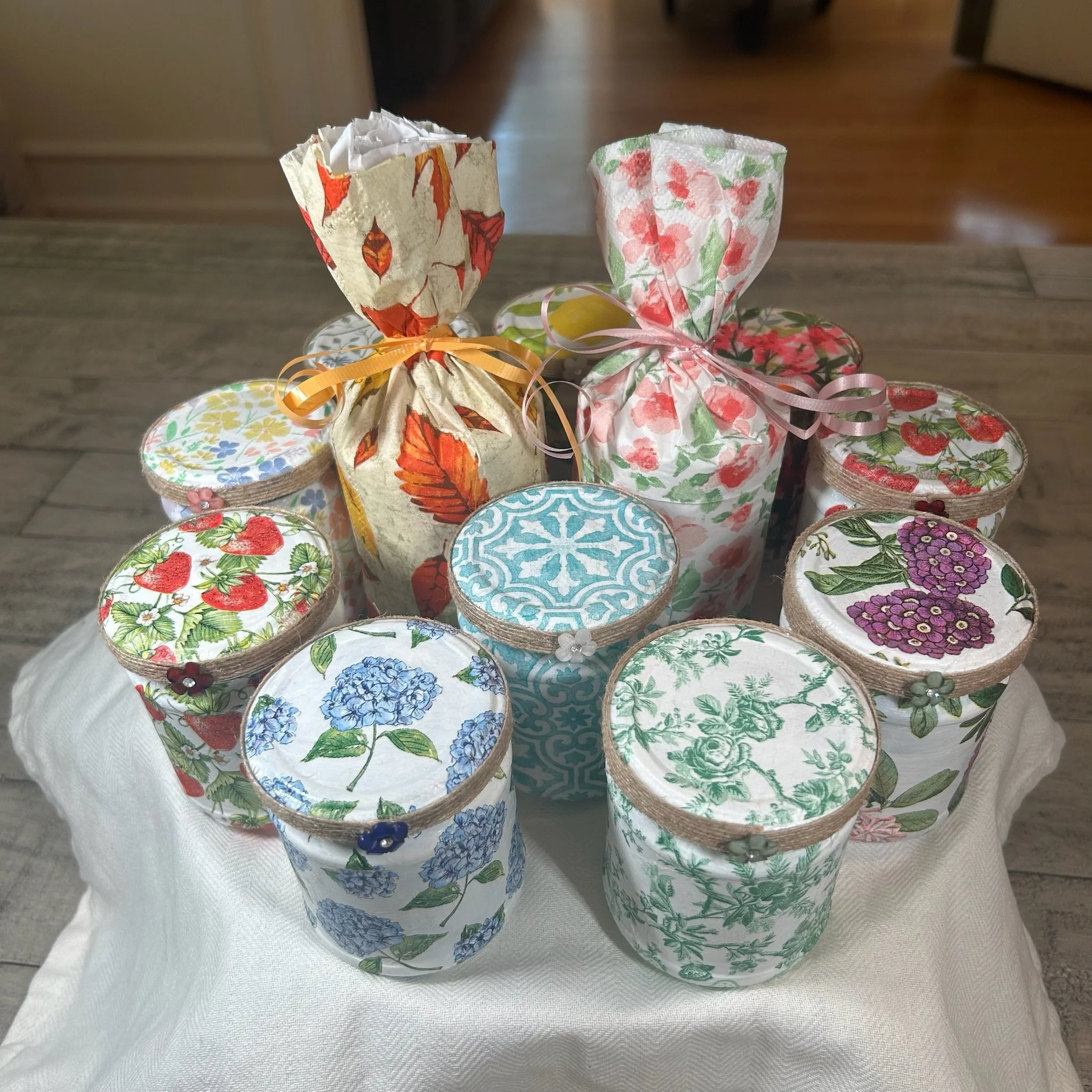 Decorative paper bags with floral and fruit patterns, tied with colorful ribbons, arranged on a table with a white tablecloth.