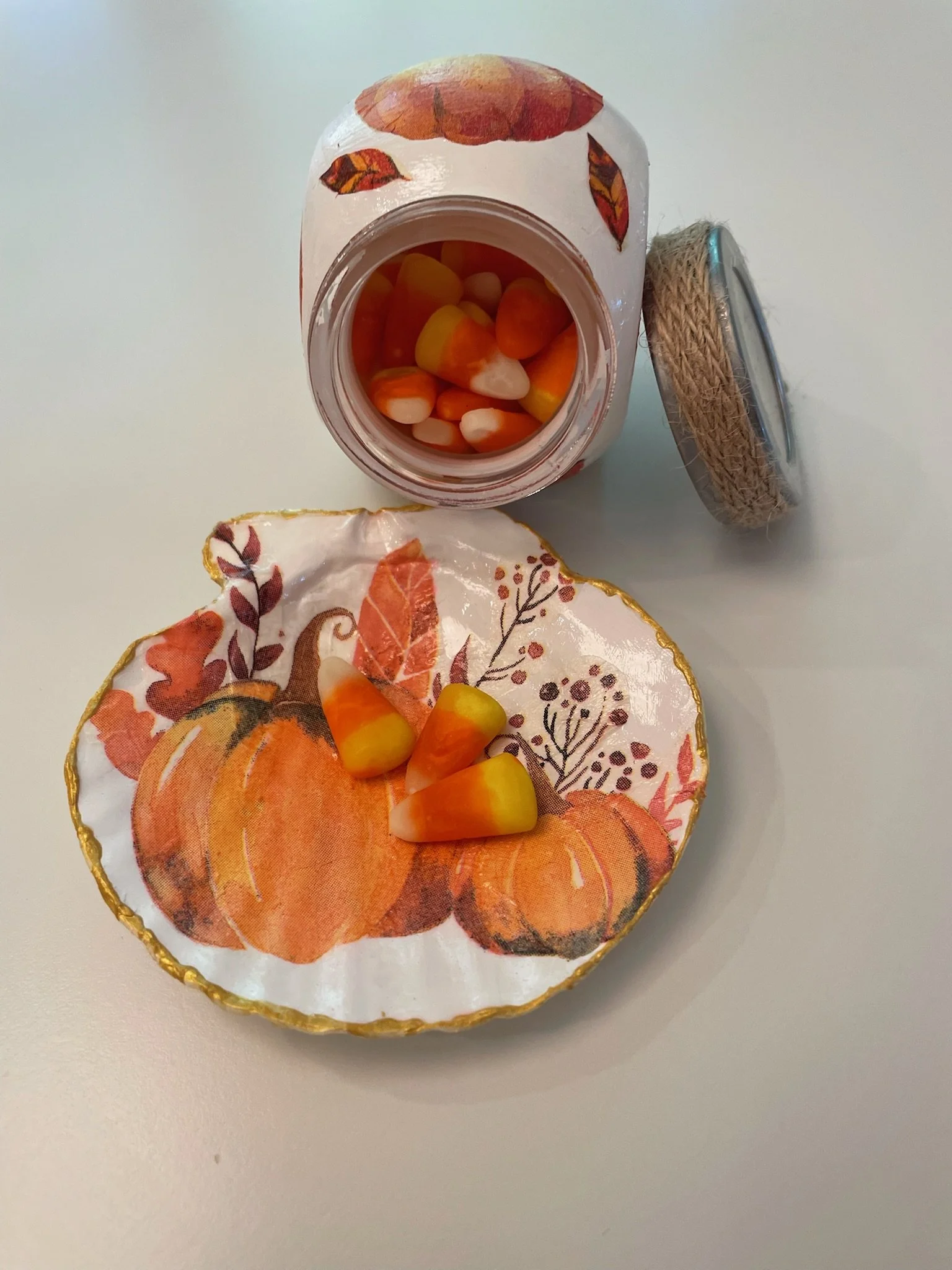 An open jar of candy corn with a decorative cover and matching plate with candy corn on a white surface.