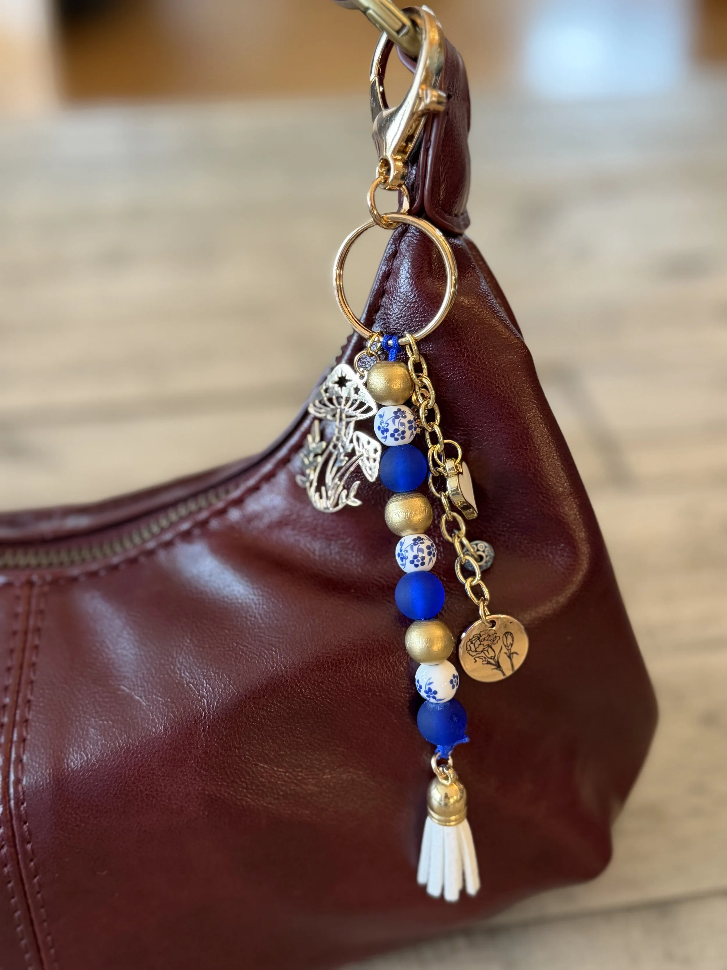 Close-up of a keychain with charms hanging from a burgundy leather bag.