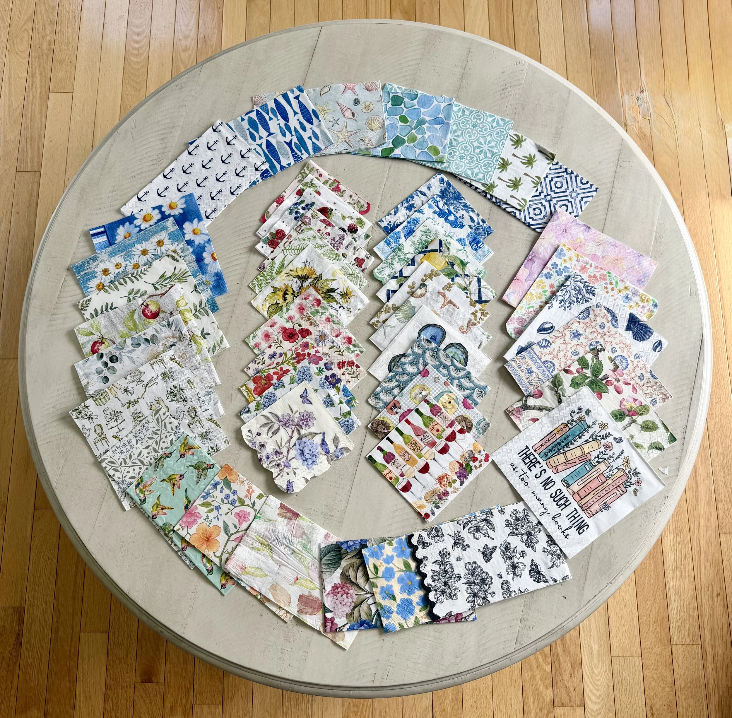 A circular arrangement of colorful fabric swatches with various floral, geometric, and nature-inspired patterns, spread out on a light-colored wooden round table.