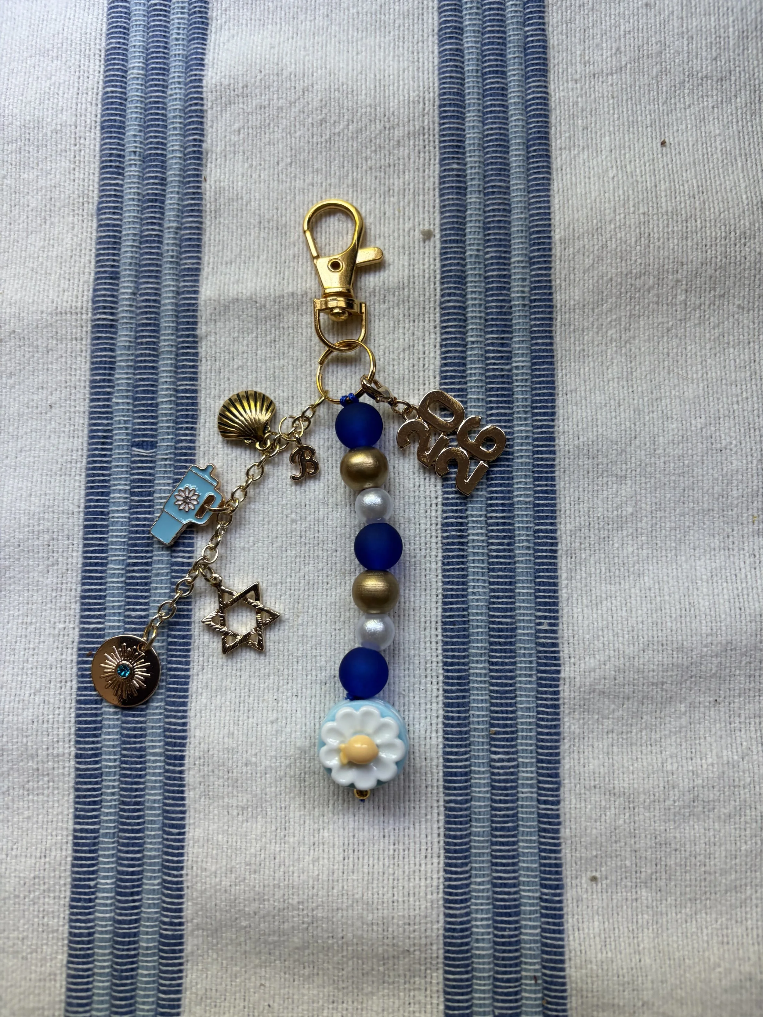 A beaded necklace with various charms and beads lying on a fabric with vertical blue stripes.