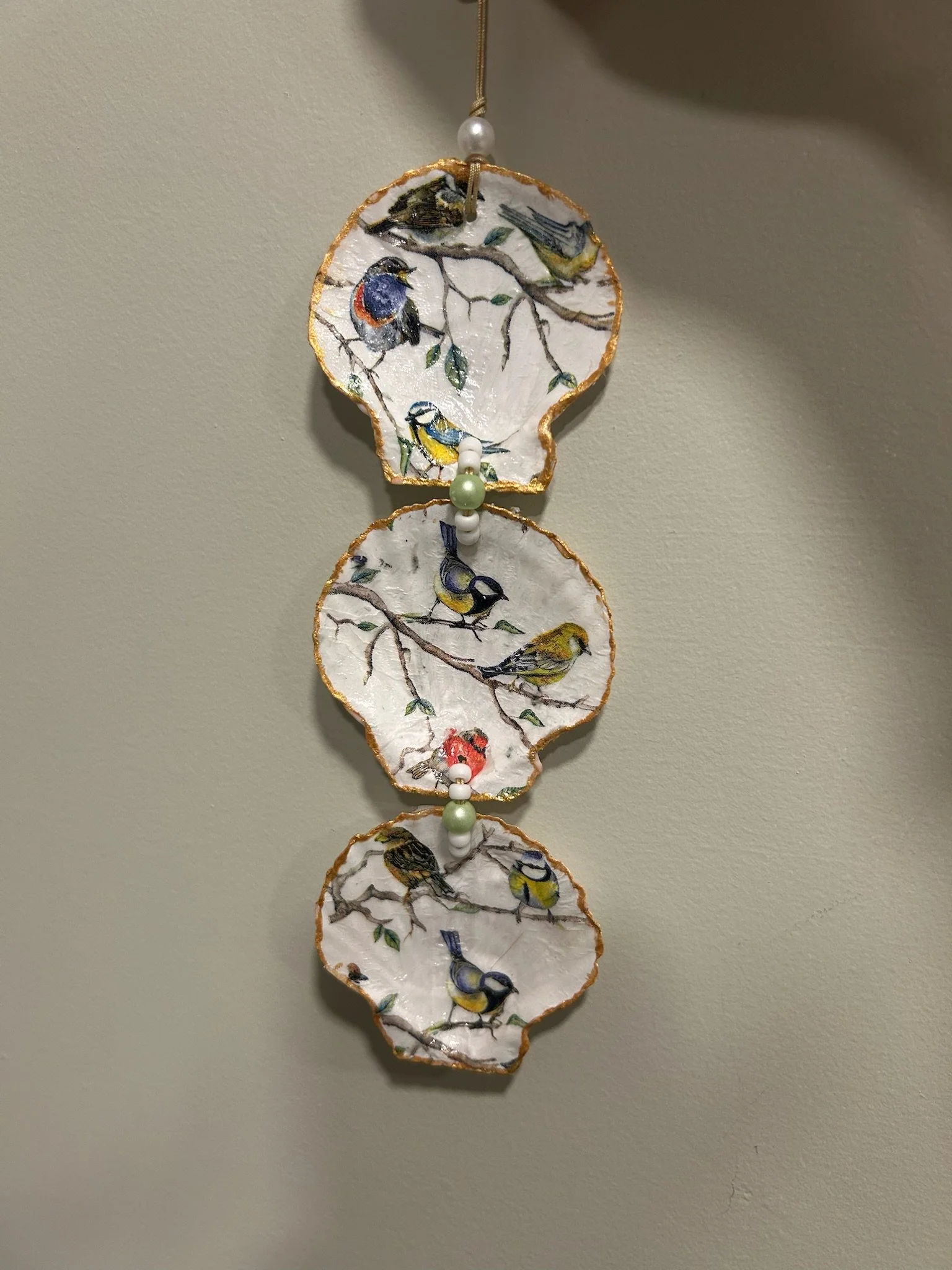 Decorative hanging wind chime made of ceramic discs, painted with colorful bird illustrations, connected with beads and a string for hanging.