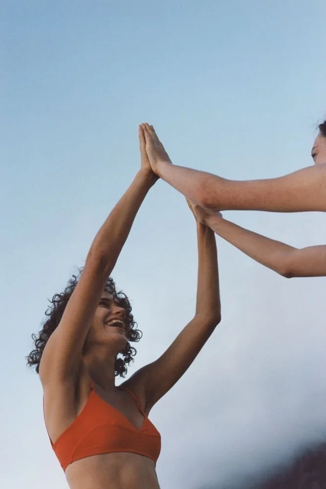 Two women giving each other a high five outdoors with a blue sky background, both smiling.