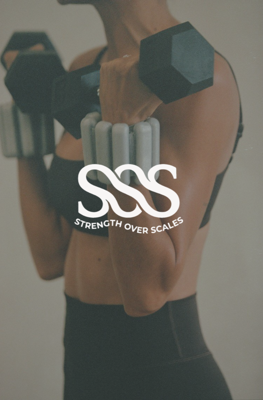 A woman holding a black hexagonal dumbbell on her shoulder, with fitness equipment visible in the background. The overlay text reads "Strength Over Scales."