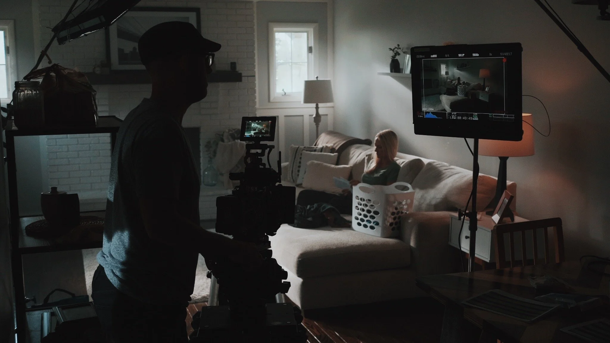 Inside a home filming scene with a woman sitting on a couch, filmed by a cinematographer, with a monitor displaying the scene, for video production in Evansville.