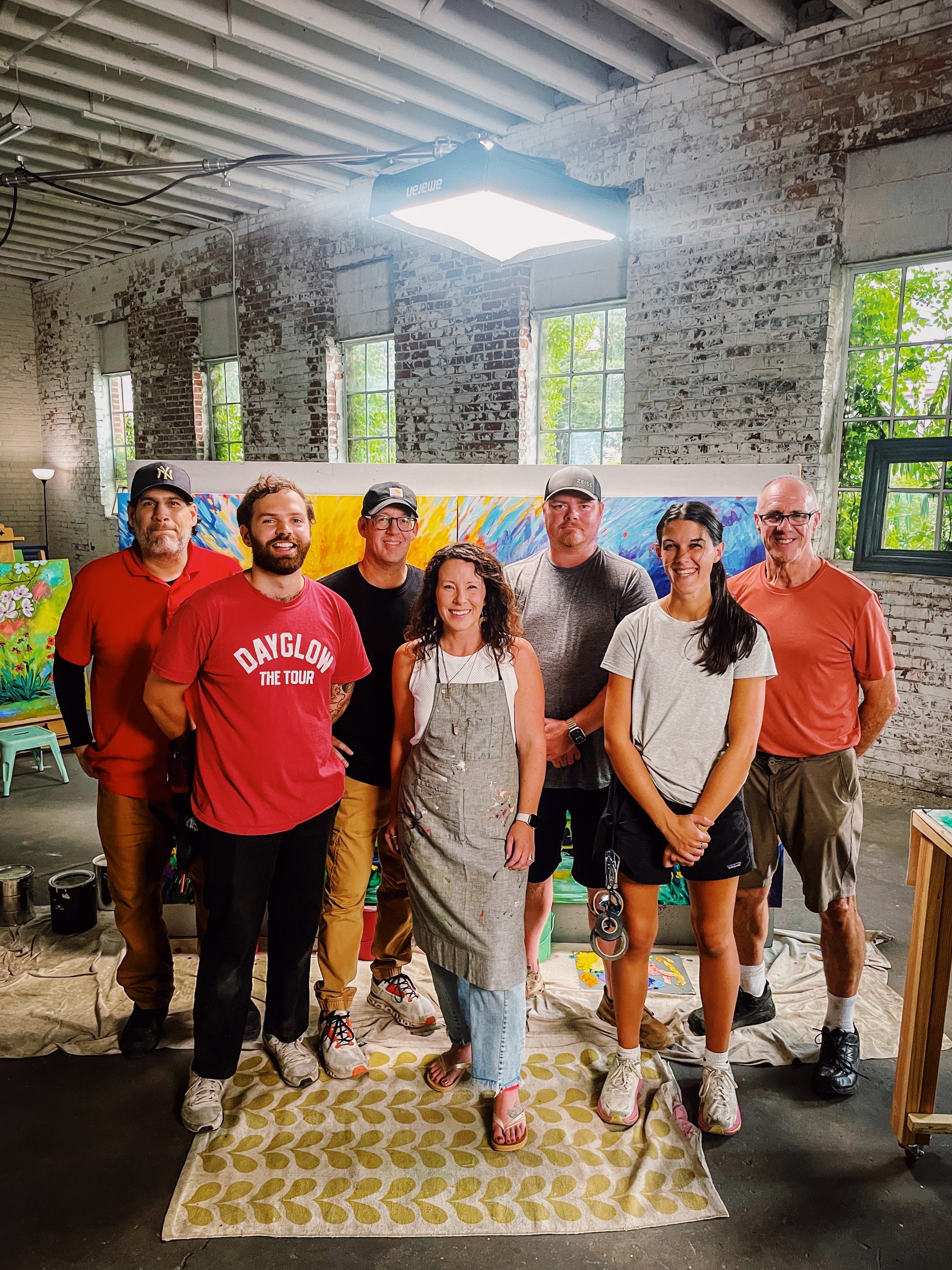 Film crew standing in an art studio with brick walls, large windows, and artworks behind them.