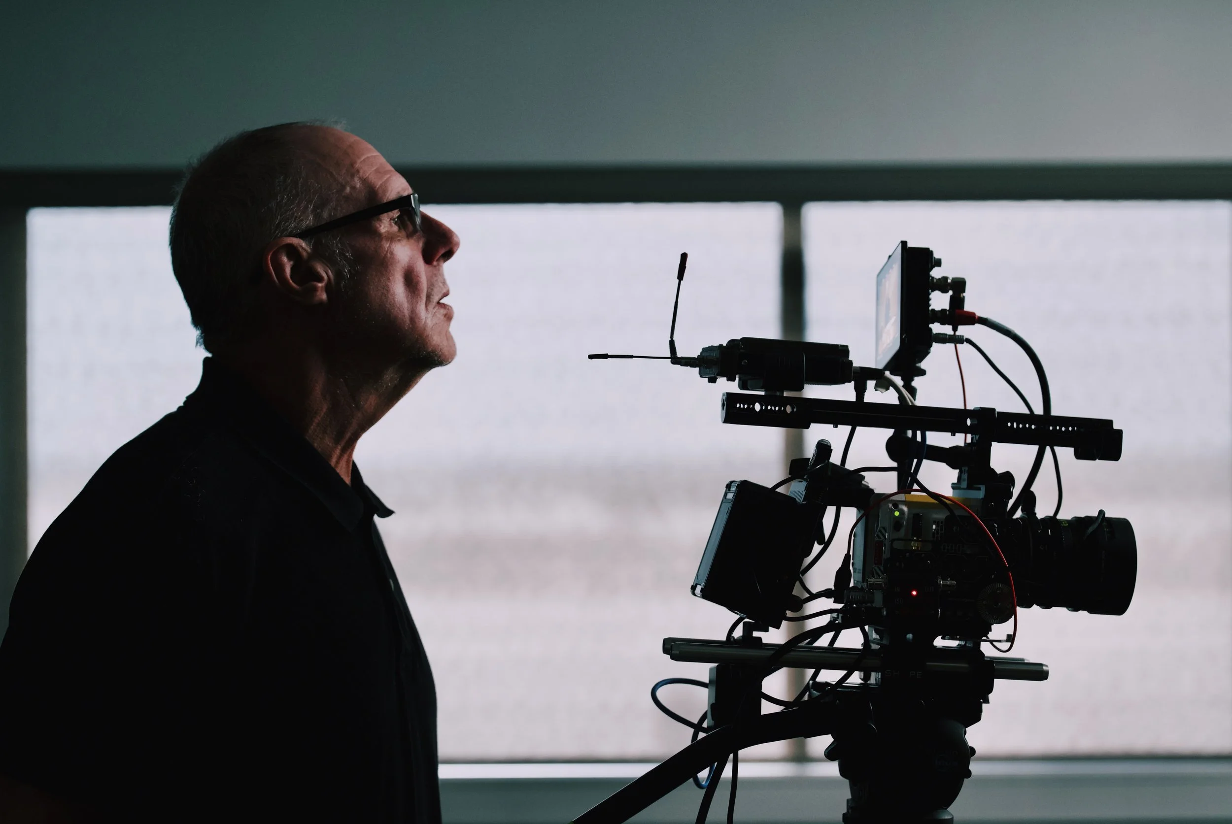 David Ross looks at a professional video camera mounted on a rig, with a window in the background.